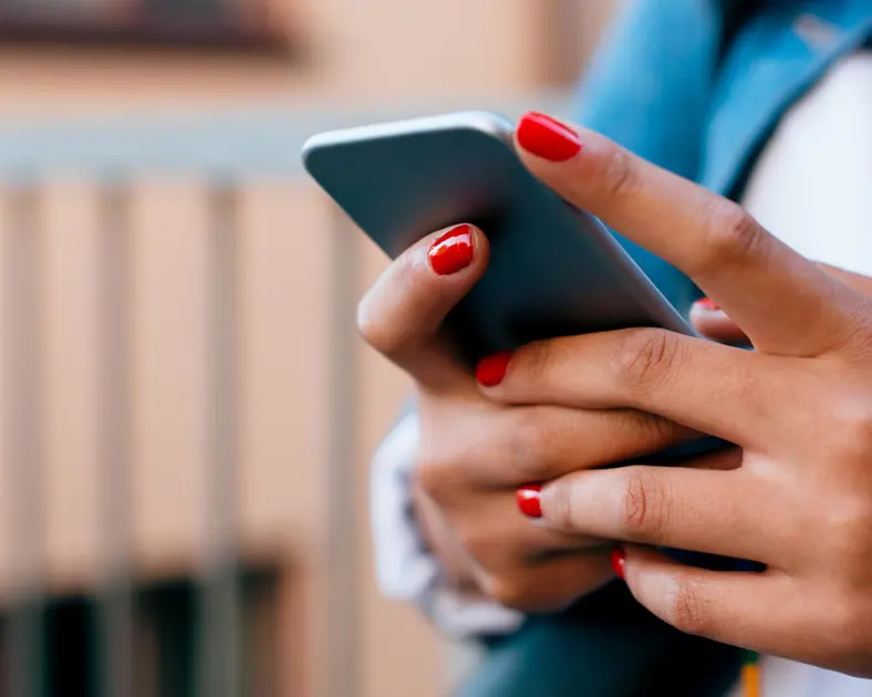 Kvinna med röda naglar håller i mobil.
