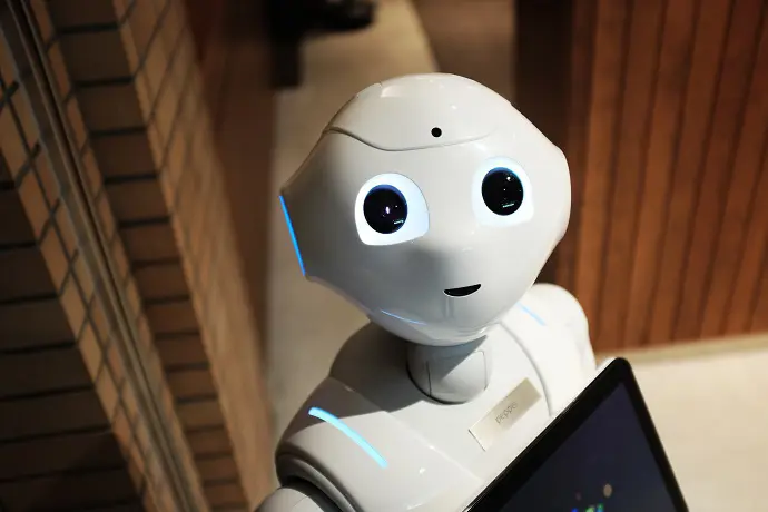Humanoid robot med vita detaljer som tittar mot kameran i en inomhusmiljö