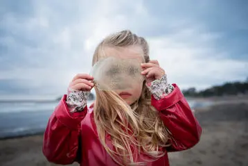 Flicka i röd jacka håller upp genomskinligt föremål vid havet