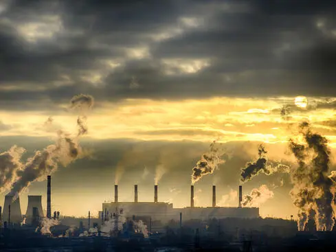 Industriell fabrik med rökstaplar som släpper ut föroreningar under en dramatisk solnedgång