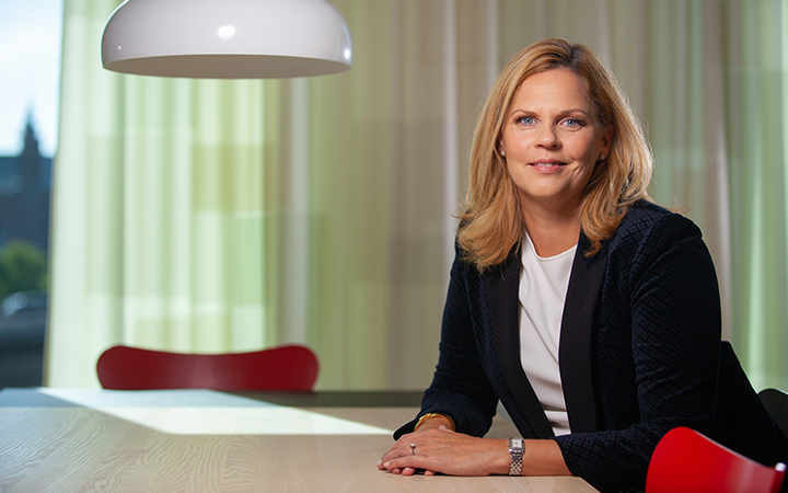 Kvinna i affärsmiljö sitter vid ett bord med modern inredning och ljusinsläpp i bakgrunden