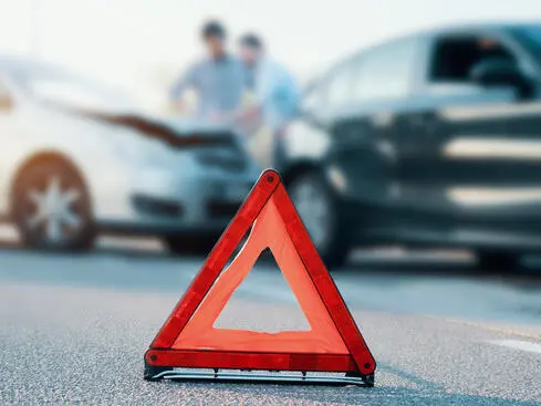 Varningstriangel på vägen med två bilar som har krockat i bakgrunden