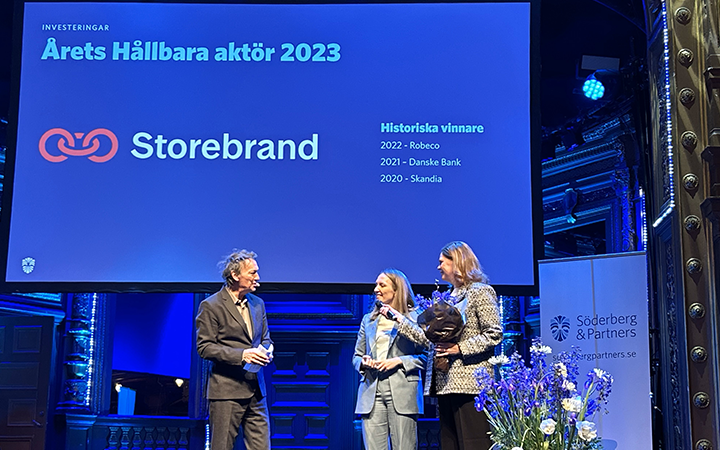 Tre personer står på scenen vid Söderberg & Partners event där Storebrand utses till "Årets Hållbara Aktör 2023". Bakgrunden visar en skärm med tidigare vinnare och eventets detaljer