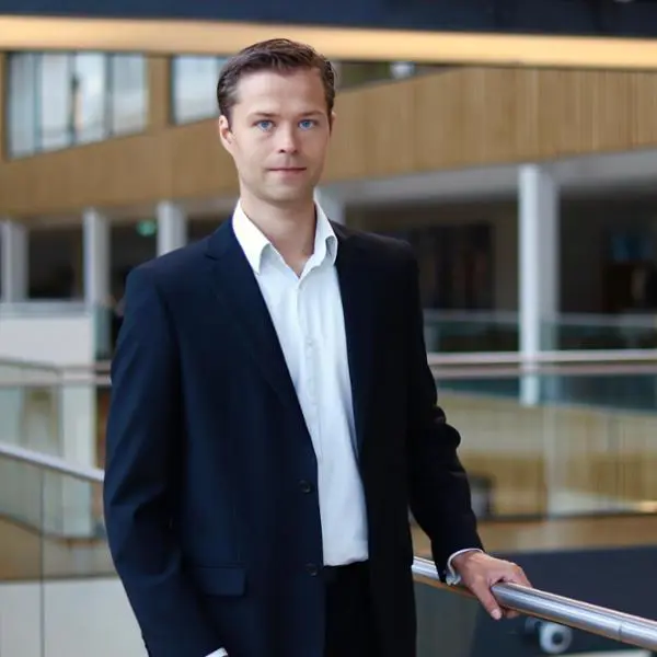 Man i mörk kostym står i modernt kontorslandskap, lutar sig mot räcke